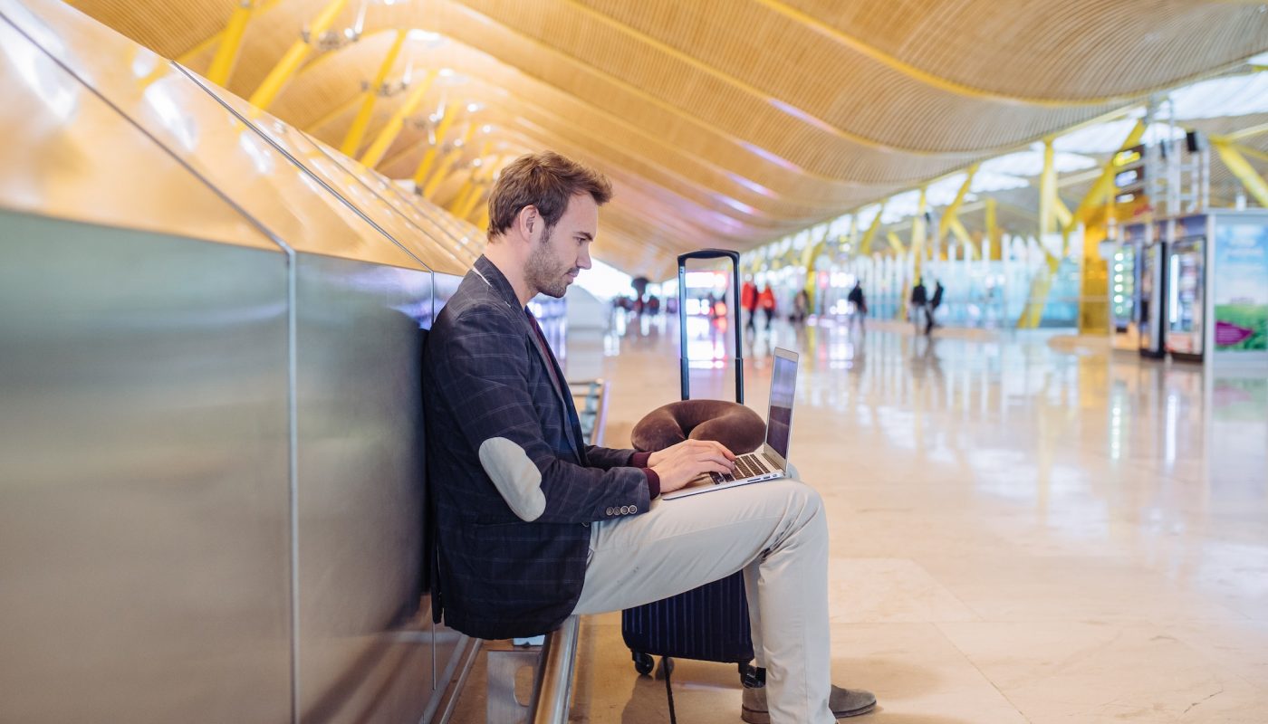 Young attractive man sitting at the airport working with a lapto