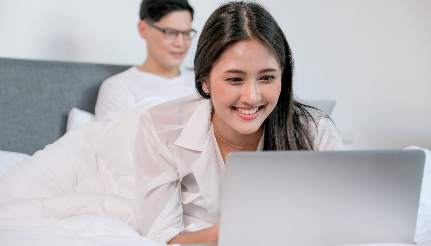 Beautiful woman use laptop on bed with smiling and man also use laptop on bed